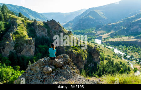 Fille assise sur un rocher à la recherche à la vue. Dans le contexte des rochers, collines, vallée. Ciel clair, collines verdoyantes, falaises escarpées, large rivière - t Banque D'Images