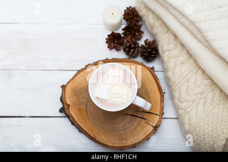 Tasse de chocolat chaud avec des guimauves, et une pile de choses tricotées sur un fond de bois blanc Banque D'Images