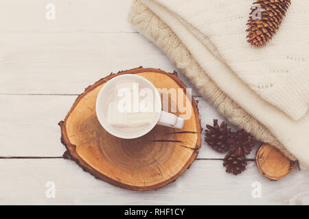 Tasse avec du chocolat chaud et des guimauves, une rangée de cônes et une pile de choses tricotées sur un fond de bois blanc Banque D'Images
