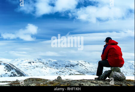 Homme assis sur les rochers à la recherche et le snow-covered hills. Ciel bleu avec des nuages. La Norvège Banque D'Images