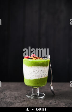Smoothie vert sain en verre. Kiwi, banane, épinards, pomme et chia smoothie graines surmontées de bleuets, framboises et amandes sur béton foncé Banque D'Images