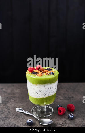 Smoothie vert sain en verre. Kiwi, banane, épinards, pomme et chia smoothie graines surmontées de bleuets, framboises et amandes sur béton foncé Banque D'Images