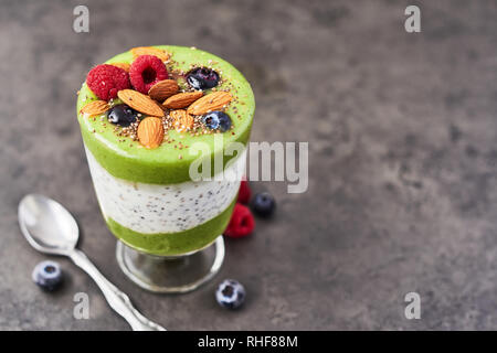 Smoothie vert sain en verre. Kiwi, banane, épinards, pomme et chia smoothie graines surmontées de bleuets, framboises et amandes sur béton foncé Banque D'Images