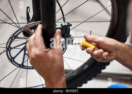 Cropped shot de mécanicien de sexe masculin travaillant dans un atelier de réparation de vélos, la réparation des freins de vélo militaire à l'aide de l'outil Banque D'Images