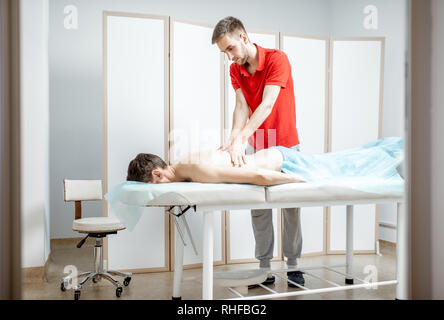 Jeune homme faisant thérapeute massage dos à un homme couché dans le livre blanc de la clinique de réhabilitation du cabinet Banque D'Images