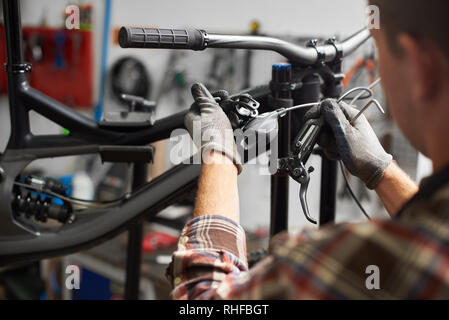 Cropped shot de réparateur professionnel travaillant en atelier de réparation de vélos, mechanic repairing bike à l'aide de l'outil, en portant des gants protecteurs Banque D'Images