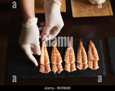 Vue rapprochée de la femme les mains dans les gants sont la préparation de crevettes sushi restaurant en roulant Banque D'Images