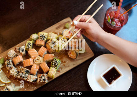 Vue rapprochée de délicieux sushis roulant servi sur la planche de bois avec des baguettes, de la sauce de soja et cocktail Banque D'Images