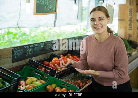 Souriante jeune femme choisissant les tomates en épicerie Banque D'Images