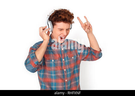 Adolescents portant des écouteurs sans fil studio isolés sur mur blanc à l'écoute de la musique rock cornes montrant le chant des gestes concentrés Banque D'Images