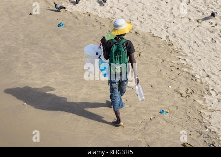 Durban, Afrique du Sud - Janvier 7th, 2019 : Un homme noir d'Afrique du Sud la collecte de bouteilles en plastique marche sur le sable dans une plage à Durban, Afrique du Sud. Banque D'Images