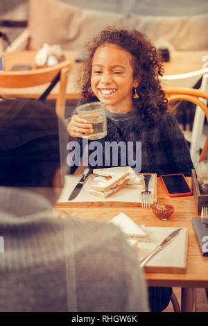 Girl laughing tandis que l'eau potable dans les restaurant et parlant avec les parents Banque D'Images