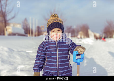 Un petit garçon dans l'hiver en ville, dans un pyjama bleu et un chapeau jaune chaud. Dans les mains de la tenue d'une spatule. Surpris au repos dans la nature l'extérieur Banque D'Images