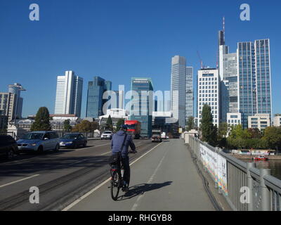 Les cycles d'un homme à travers le pont Untermainbrücke vers les skyscapers du quartier financier, par temps clair, à Francfort en 2018. Banque D'Images