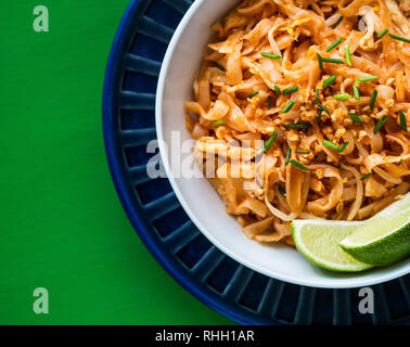 Vue aérienne de white bol de nouilles Pad Thaï au poulet et garnir de chaux, sur la plaque bleu et vert surface. Banque D'Images