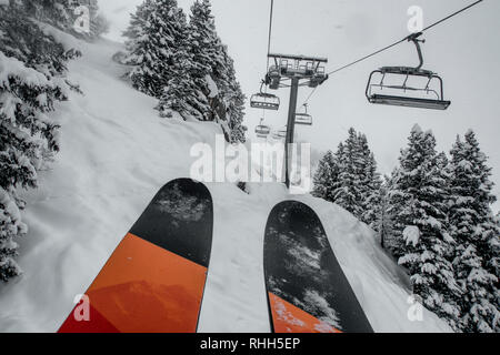 Télésiège de ski skieurs et planchistes portant jusqu'à la montagne pendant les fortes chutes de neige sur une journée d'hiver brumeux à Courchevel, France. Banque D'Images