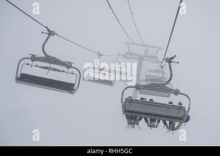 Télésiège de ski skieurs et planchistes portant jusqu'à la montagne pendant les fortes chutes de neige sur une journée d'hiver brumeux à Courchevel, France. Banque D'Images