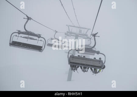 Télésiège de ski skieurs et planchistes portant jusqu'à la montagne pendant les fortes chutes de neige sur une journée d'hiver brumeux à Courchevel, France. Banque D'Images