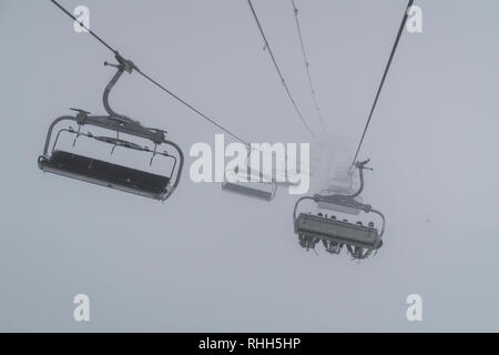 Télésiège de ski skieurs et planchistes portant jusqu'à la montagne pendant les fortes chutes de neige sur une journée d'hiver brumeux à Courchevel, France. Banque D'Images