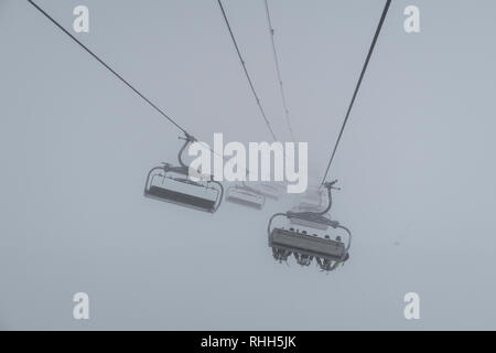 Télésiège de ski skieurs et planchistes portant jusqu'à la montagne pendant les fortes chutes de neige sur une journée d'hiver brumeux à Courchevel, France. Banque D'Images