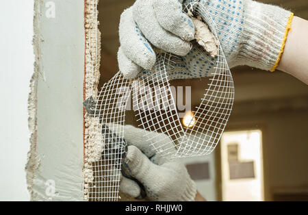 Un travailleur est couper un morceau de filet de fibre de verre avec un couteau pendant une rénovation appartement Banque D'Images