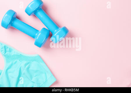 Soutien-gorge sport et haltères bleu sur fond rose, vue du dessus avec l'exemplaire de l'espace. Concept de remise en forme Banque D'Images