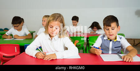 Groupe d'élèves du primaire assis à un bureau et effectuer les tâches en classe Banque D'Images