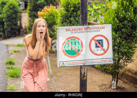 BALI, INDONÉSIE - 21 mai, 2018 : Jeune femme regarde signe de protestation sur un mur en indonésien s'opposer à l'Uber et saisir les chauffeurs de taxi se lit 'Uber et saisir Banque D'Images