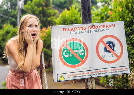 BALI, INDONÉSIE - 21 mai, 2018 : Jeune femme regarde signe de protestation sur un mur en indonésien s'opposer à l'Uber et saisir les chauffeurs de taxi se lit 'Uber et saisir Banque D'Images