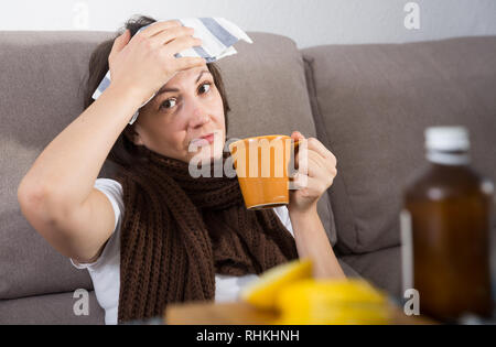 Femme souffrant de maux de tête et fièvre au canapé à la maison Banque D'Images