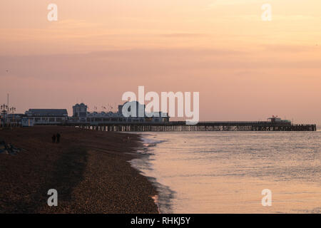 Un couple se réveiller le long de la plage de galets au front de mer de Southsea pendant le coucher du soleil avec south parade pier dans l'arrière-plan Banque D'Images