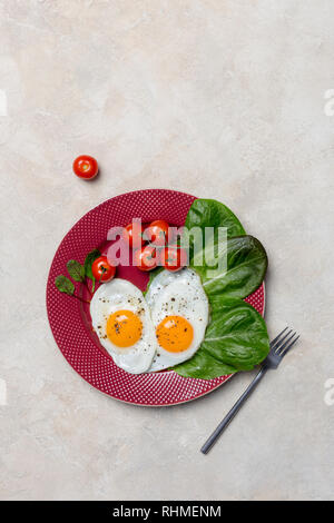 Forme du cœur deux oeufs au plat avec salade de tomates cerises et romano à la fourchette avec plaque rouge sur fond blanc. Concept vertical d'aliments sains. Free s Banque D'Images