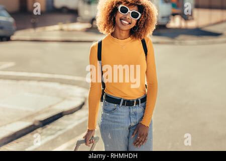 Femme afro-américain en vacances, marcher autour de la ville. Femme portant des lunettes de soleil et un sac à dos marche sur rue. Banque D'Images