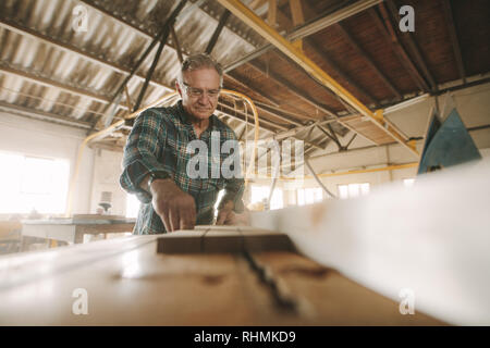 Senior male carpenter la coupe de bois sur le tableau a vu la machine. Young caucasian man travaillant en atelier de menuiserie. Banque D'Images