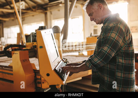 Senior male carpenter la programmation d'une machine à bois cnc en atelier. Homme mûr prépare un programme d'ordinateur pour machine à commande numérique à l'atelier de menuiserie Banque D'Images