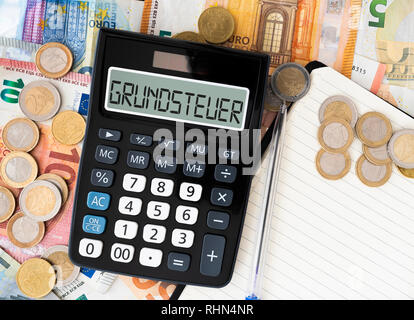 Mot allemand Grundsteuer (l'impôt foncier ou taxe foncière) sur l'affichage de la calculatrice de poche avec l'introduction des billets et des pièces en arrière-plan Banque D'Images
