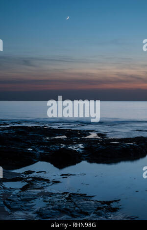 Constantine Bay, à Cornwall, en Angleterre, au crépuscule avec la Lune se levant sur la mer. Banque D'Images