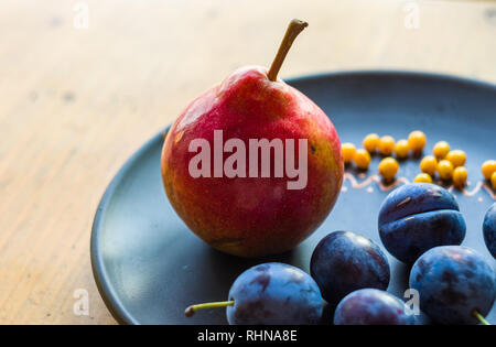 Still Life - prunes juteuses, grand bleu, de poire mûre et de petits fruits de l'argousier dans une plaque en céramique sur un fond de bois, close-up Banque D'Images