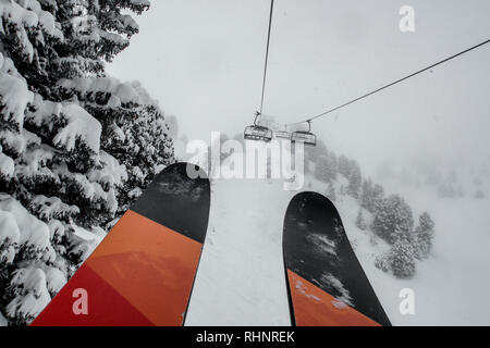 Télésiège de ski skieurs et planchistes portant jusqu'à la montagne pendant les fortes chutes de neige sur une journée d'hiver brumeux à Courchevel, France. Banque D'Images