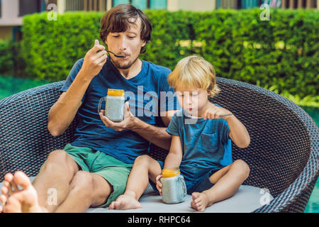Père et fils manger le dessert avec chia seeds et de mangues à la piscine le matin. la saine alimentation, l'alimentation, les régimes végétariens et personnes concept Banque D'Images