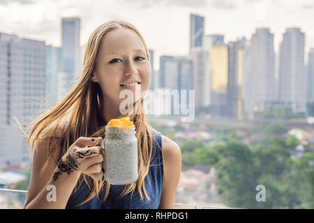 Jeune femme avec de l'henné mehendi sur part manger chia pudding sur son balcon donnant sur la grande ville Banque D'Images