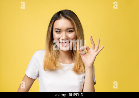 Jeune femme asiatique avec des gestes plus isoler signe ok fond jaune. Banque D'Images