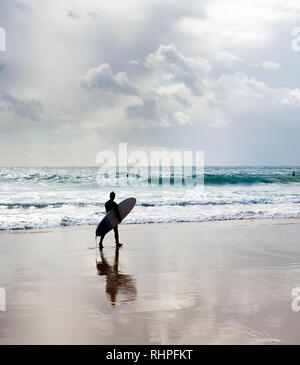 Surf surfer avec la marche sur la plage au coucher du soleil. Algarve, Portugal Banque D'Images