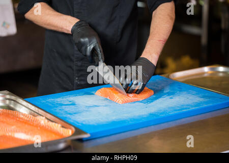 Cuisine à thème est une profession de la cuisson. Close-up of a Young Man's hand dans un restaurant de cuisine préparer les filets de poisson rouge en viande saumon noir l Banque D'Images