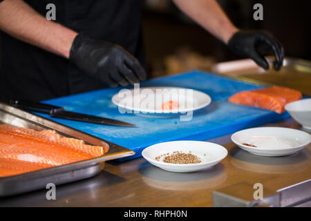 Cuisine à thème est une profession de la cuisson. Close-up of a Young Man's hand dans un restaurant de cuisine préparer les filets de poisson rouge en viande saumon noir l Banque D'Images