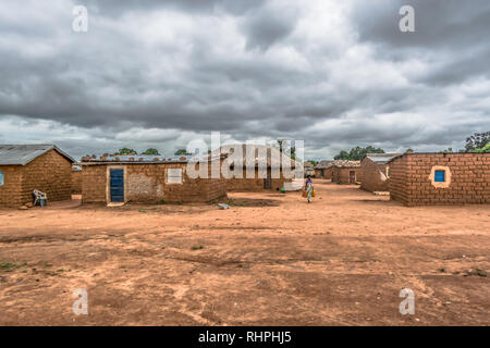 Malange / Angola - 1208 2018 : vue sur village traditionnel, femme transportant des conteneurs d'eau sur chemin, maisons d'adobe avec toit et d'ocre et stra Banque D'Images