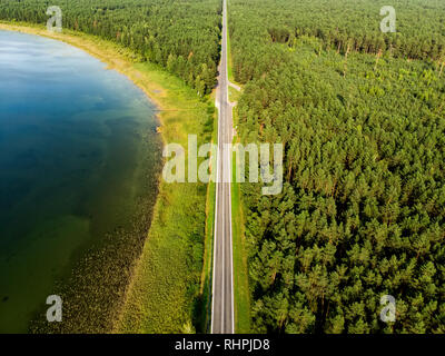 Vue aérienne de haut en bas de la route à deux voies avec des forêts de pins d'un côté, et le lac d'un vert profond sur l'autre. Beau paysage d'été en Lituanie. Banque D'Images