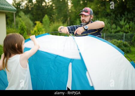 Cute little girls à aider leurs parents à mettre en place une tente sur un camping. Mode de vie actif, week-end, loisirs de plein air d'été. Banque D'Images