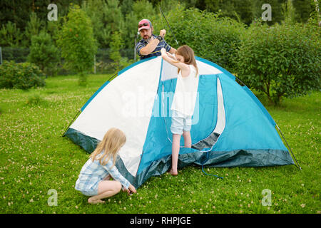 Cute little girls à aider leurs parents à mettre en place une tente sur un camping. Mode de vie actif, week-end, loisirs de plein air d'été. Banque D'Images