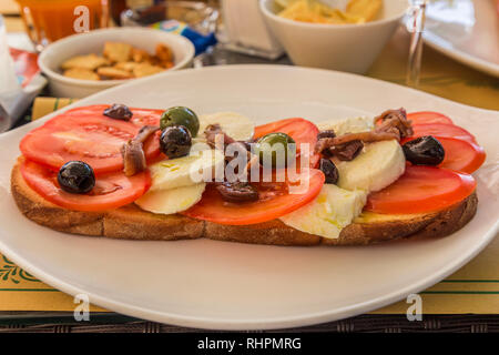 Collation au déjeuner de tomates, olives et fromage. anchois sur du pain, servi sur une plaque blanche. Banque D'Images
